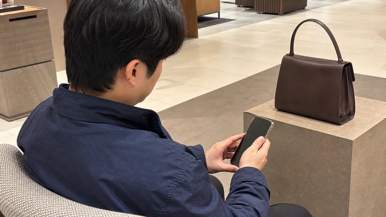 백화점 상담 전에 휴대전화로 가방 제품 정보와 구매 조건을 확인하는 모습