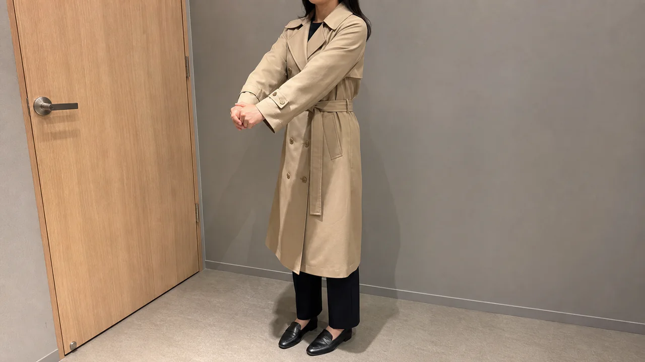 베이지 트렌치코트를 입고 팔을 앞으로 뻗어 어깨와 소매 여유를 확인하는 모습